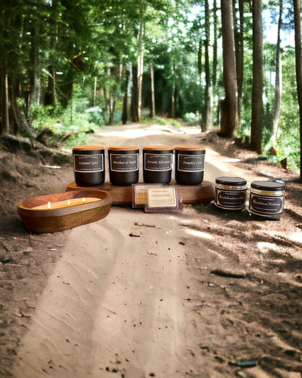 Wood wick candles, wax melts and a wood dough bowl candle sitting on a dusty road in the woods